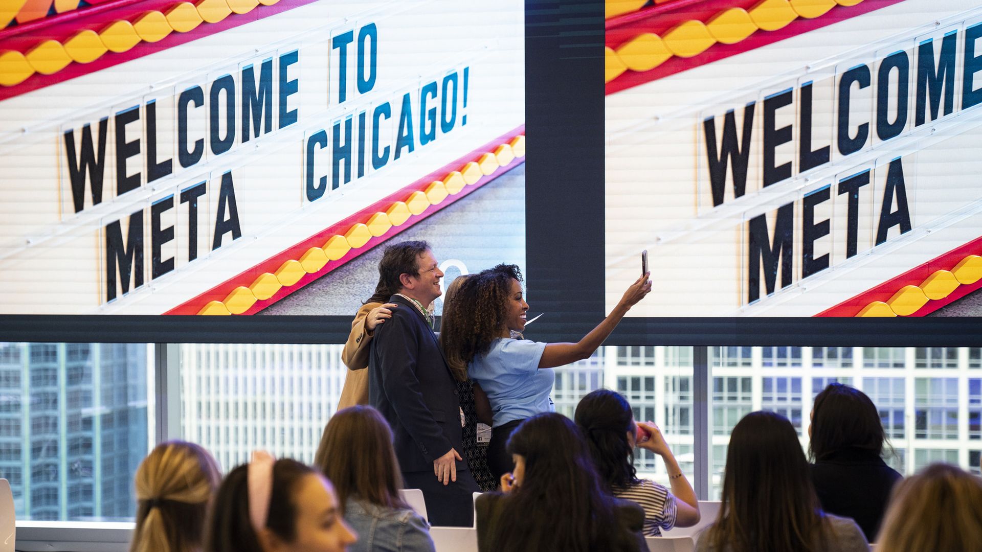 Photo of people taking selfies in front of a big sign. 