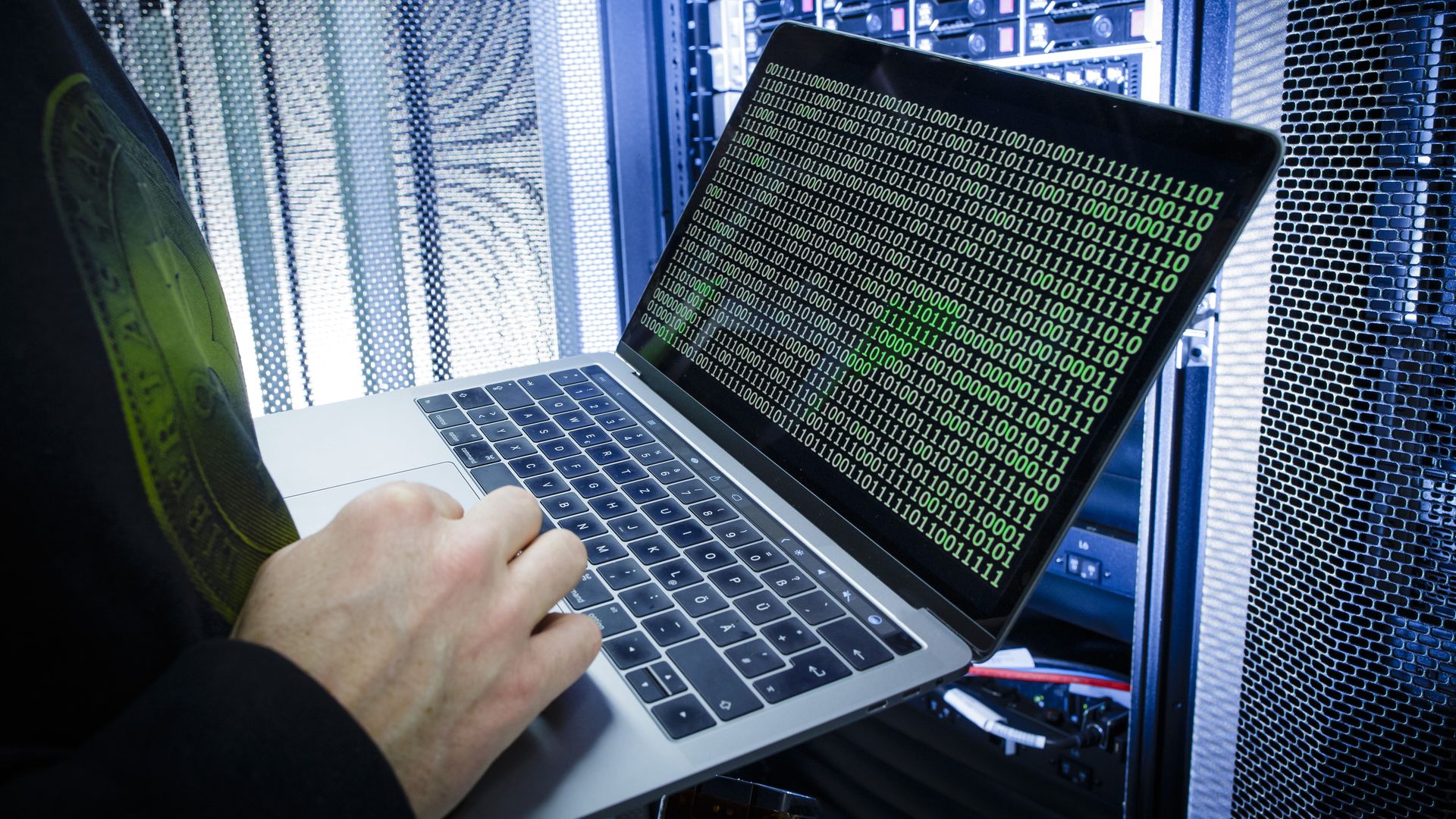 A man types on a computer with green zeroes and ones visualized