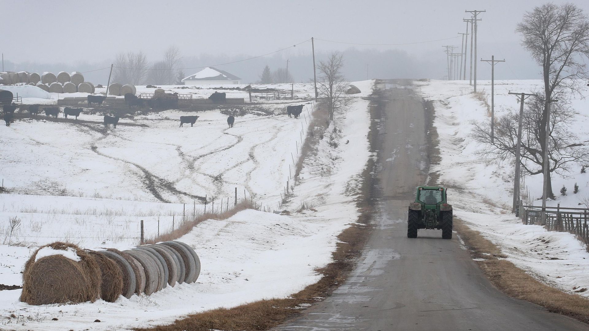In this image, a tractor drives away from the camera on a snowy one-lane road.