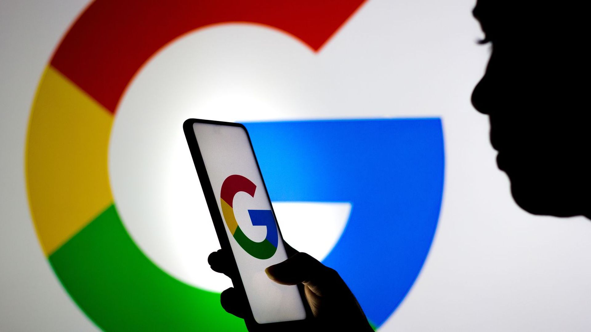 A photo illustration of a person using a smartphone with a Google logo against a background with another Google logo