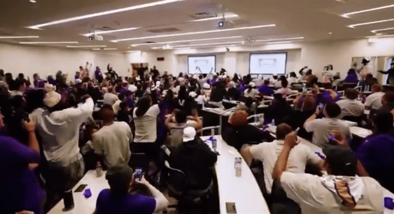 a video of the the JMU football team cheering, jumping up and down and throwing purple streamers