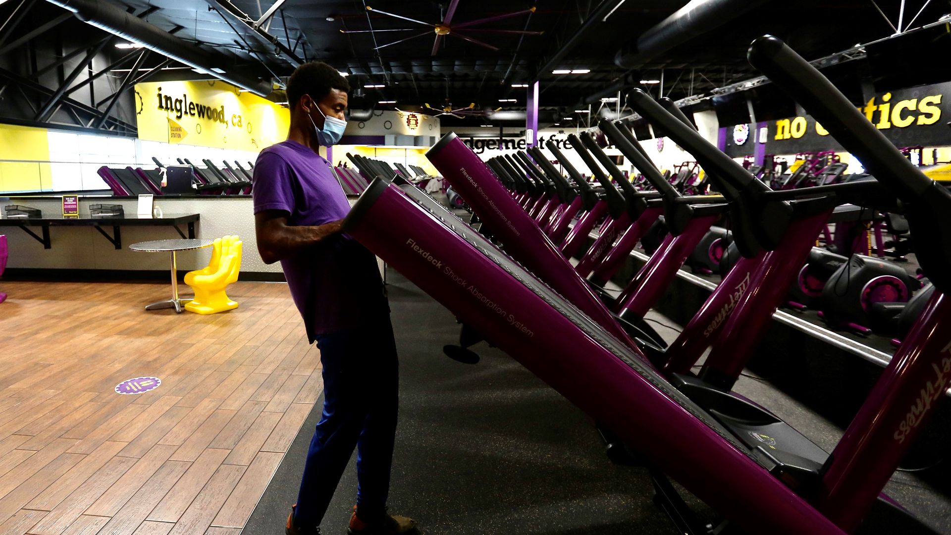 A worker unfurls a folded-up treadmill at a Planet Fitness location.