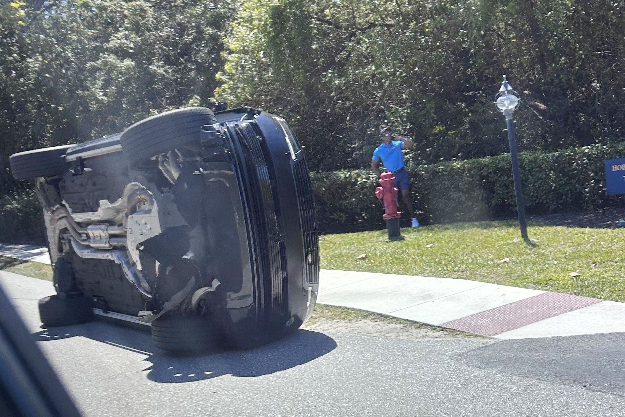 Golfer Tiger Woods stands by his overturned vehicle in Jupiter Island, Fla., on Friday, March 27, 2026. (AP Photo/Jason Oteri)
