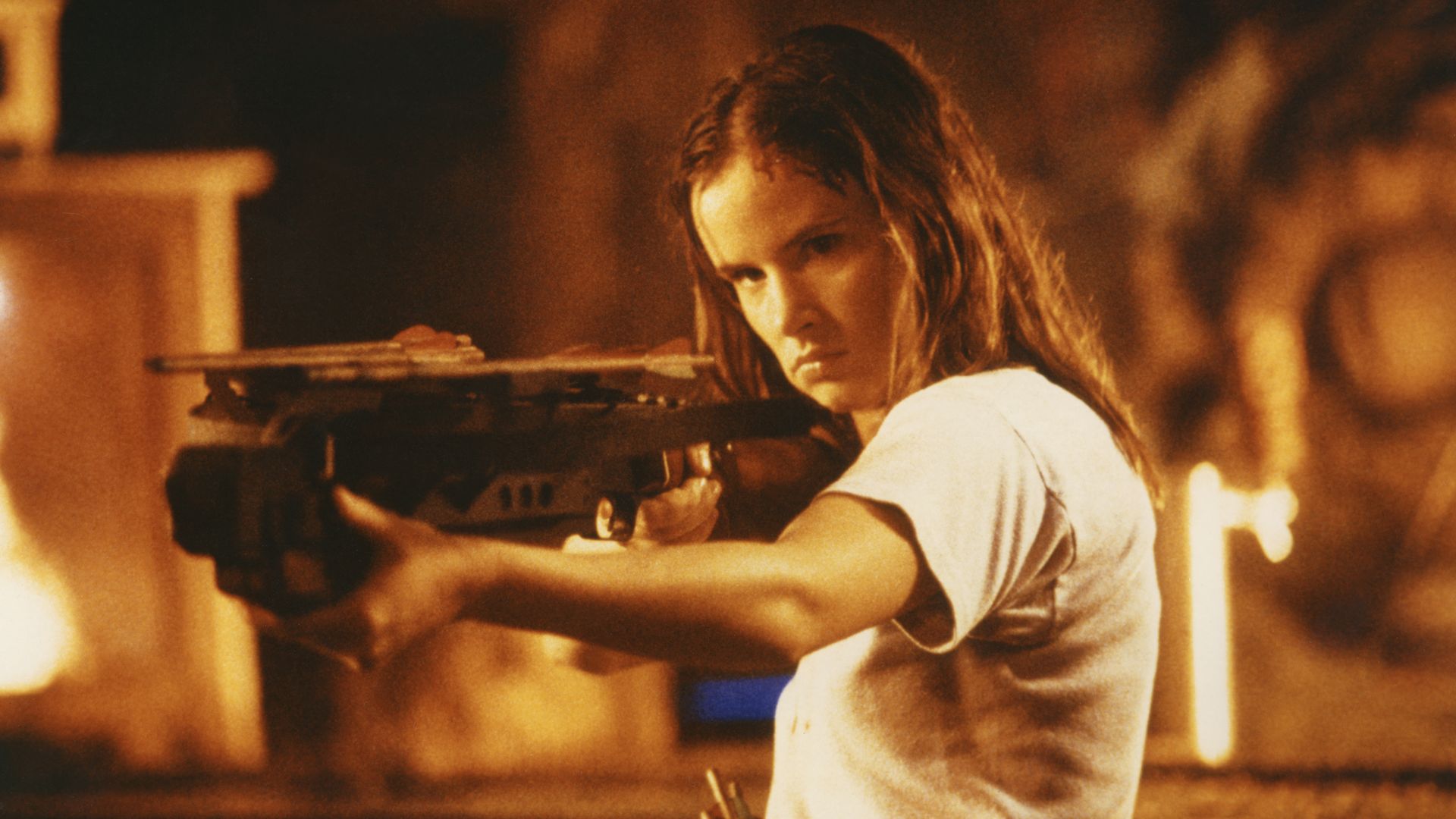 A girl holds a gun against vampires with fire in the background in this movie still. 
