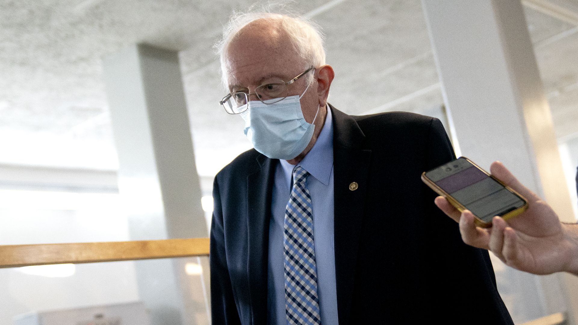 Bernie Sanders wears a suit and tie while someone holds a phone up to him. 