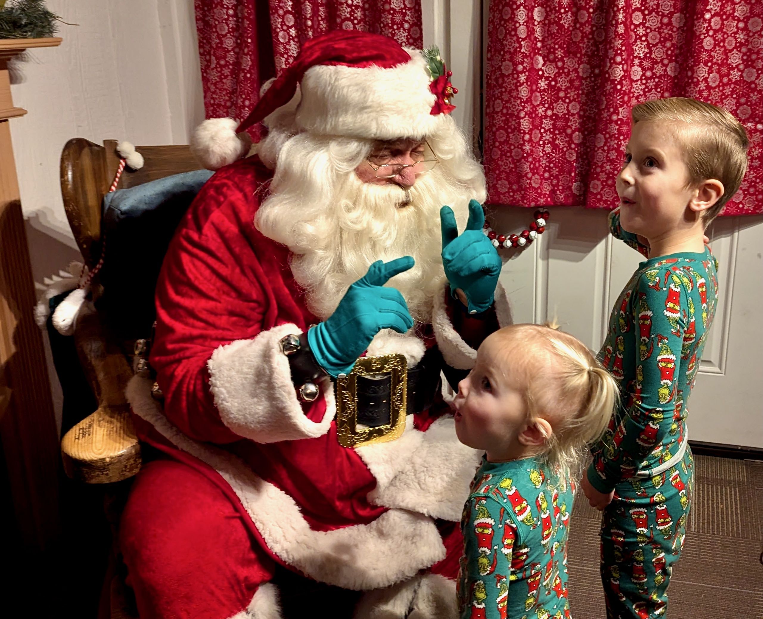 Two small children in Christmas pajamas meet Santa Claus.