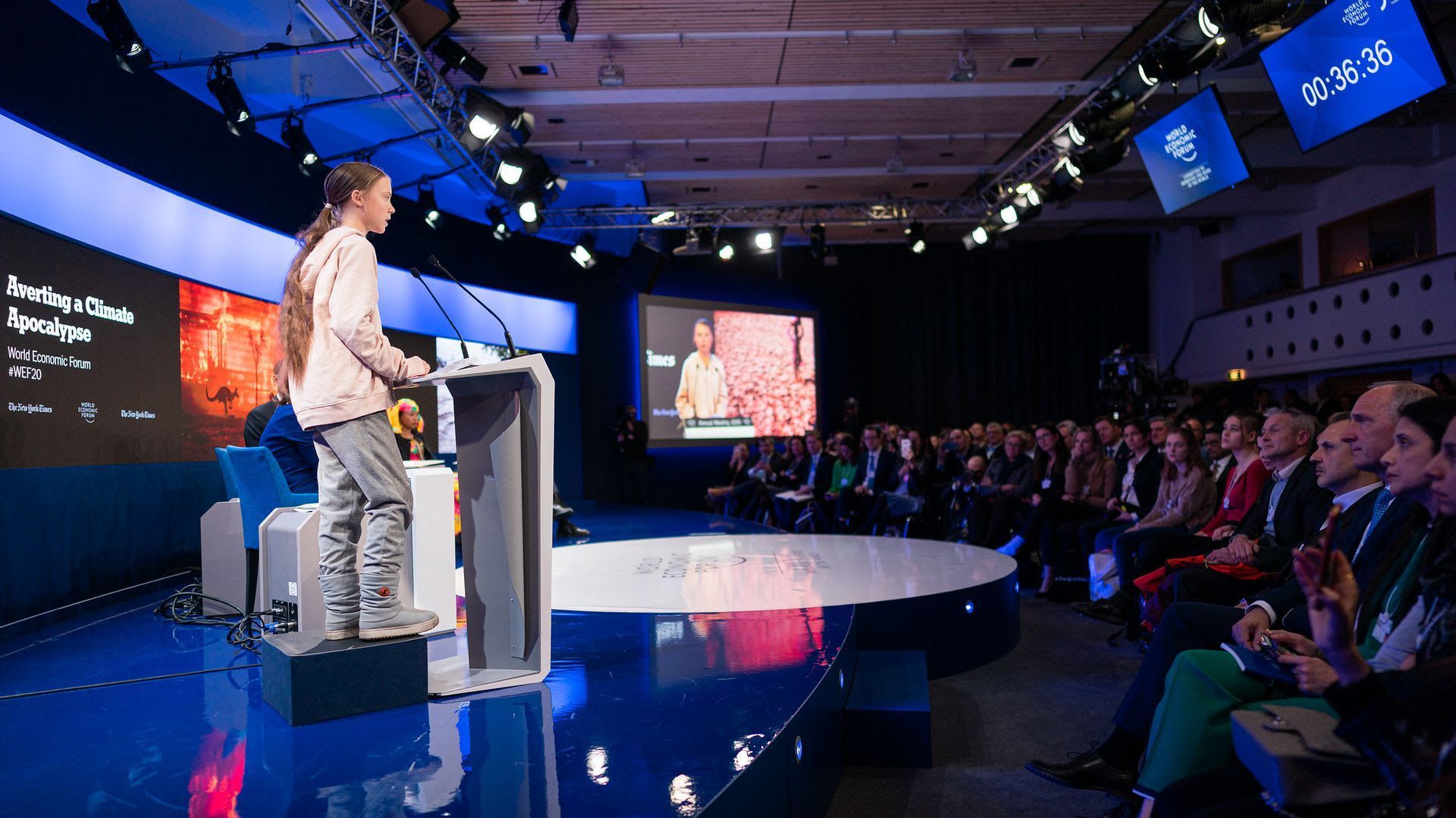 Photo of Greta Thunberg standing on a box to speak at a podium wearing animal-free clothes