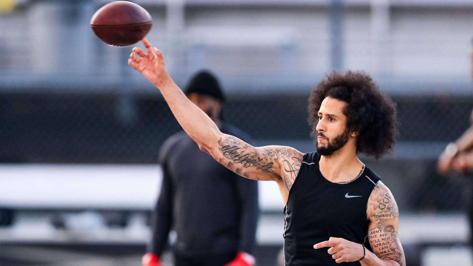 In this image, Colin Kaepernick tosses a football on a football field 
