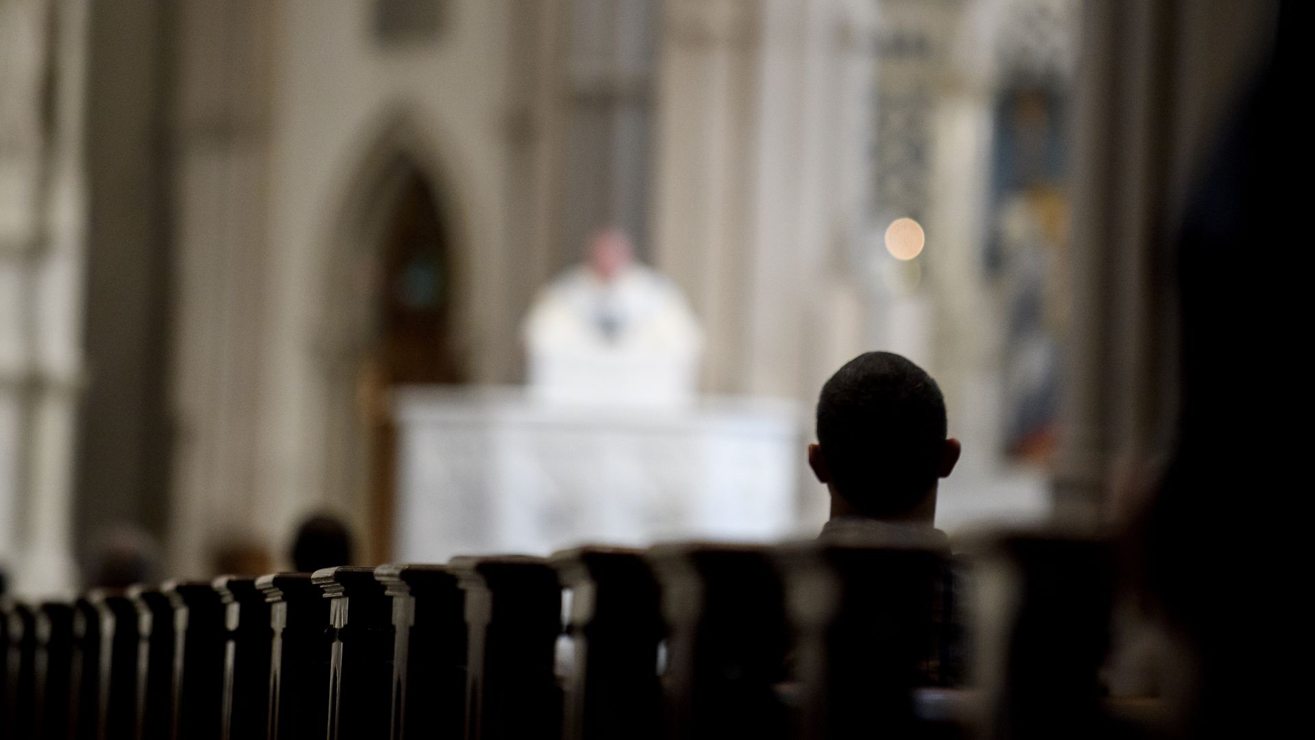 Catholic mass shows silhouetted figure in pews.