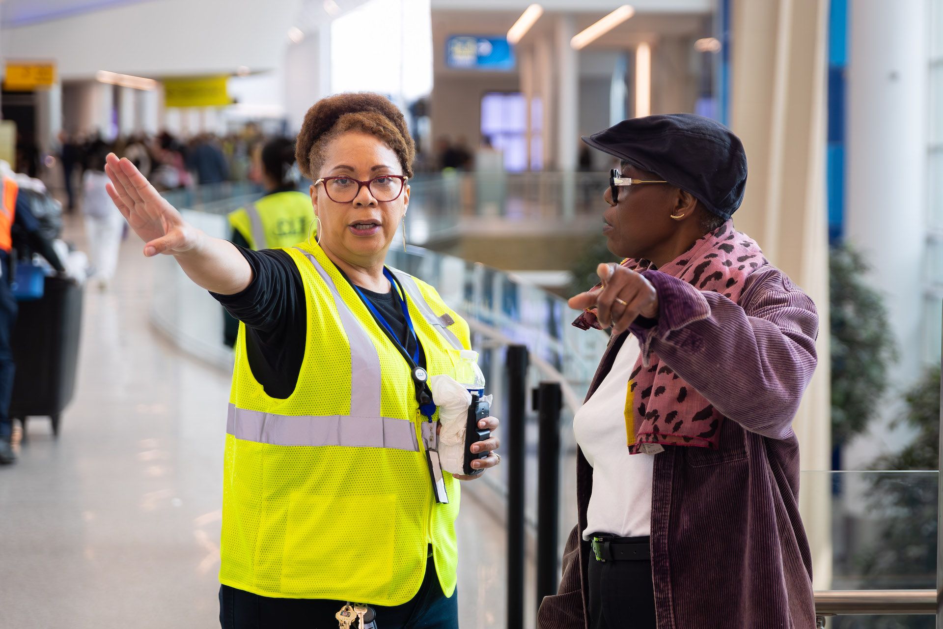 A woman in a neon yellow safety vest is giving instructions to another woman. They are inside. 