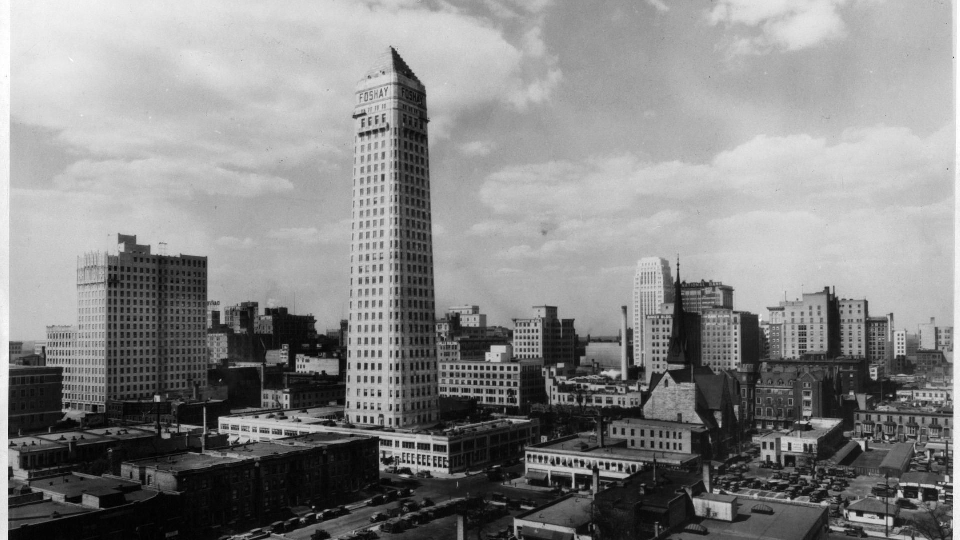 A black and white photo of The Foshay Tower, rising up over small buildings 