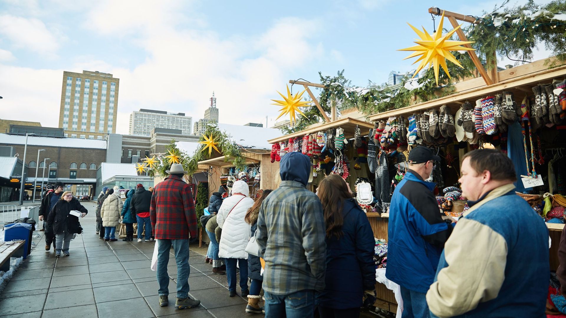 A group of people standing outside a small wooden stand that is decorated with greenery and stars.