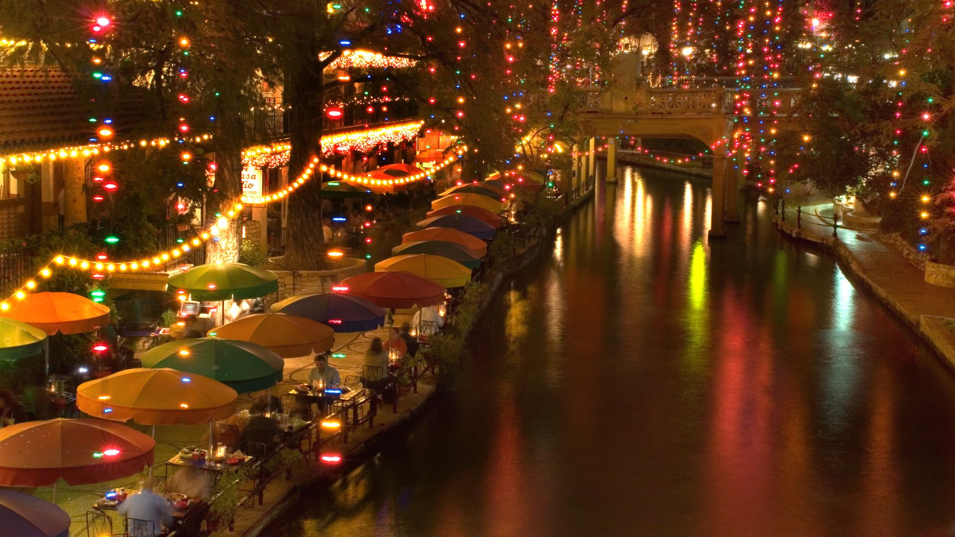 San Antonio's River Walk at night, decorated for the holidays with lights draped over trees lining the water.