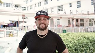 Mat "Kush" Kuscher se tient devant l'hôtel Clevelander par une journée ensoleillée portant une casquette de baseball qui dit "Miami." 