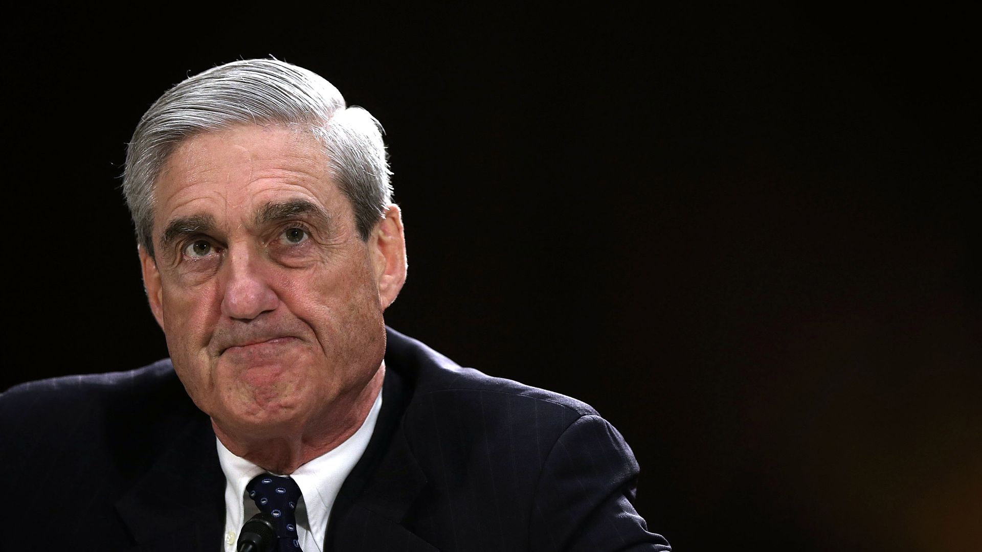Bob Mueller before a black background grimaces.
