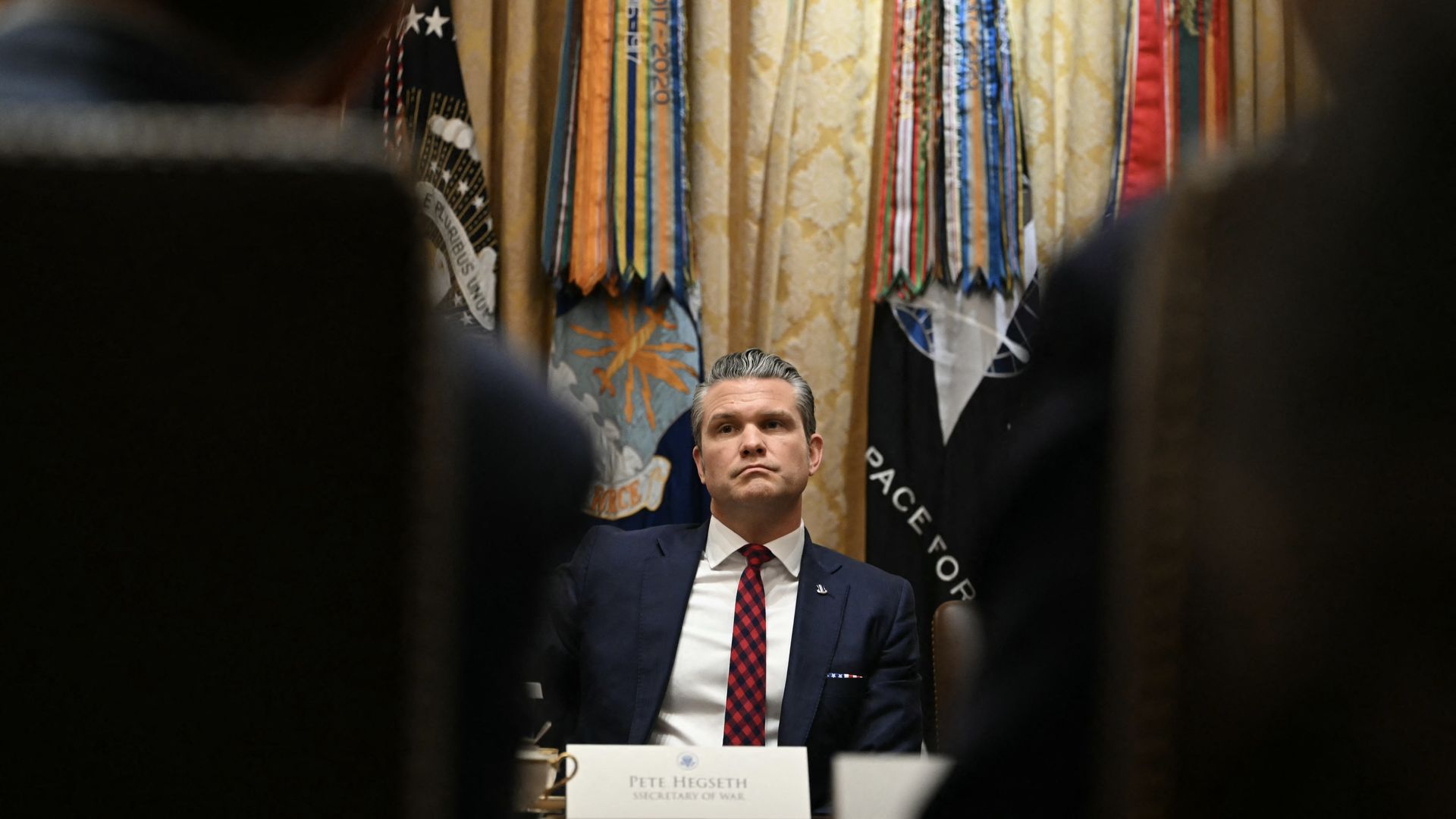 Pete Hegseth, wearing a dark suit and a red tie, sits at a table during a Cabinet meeting.