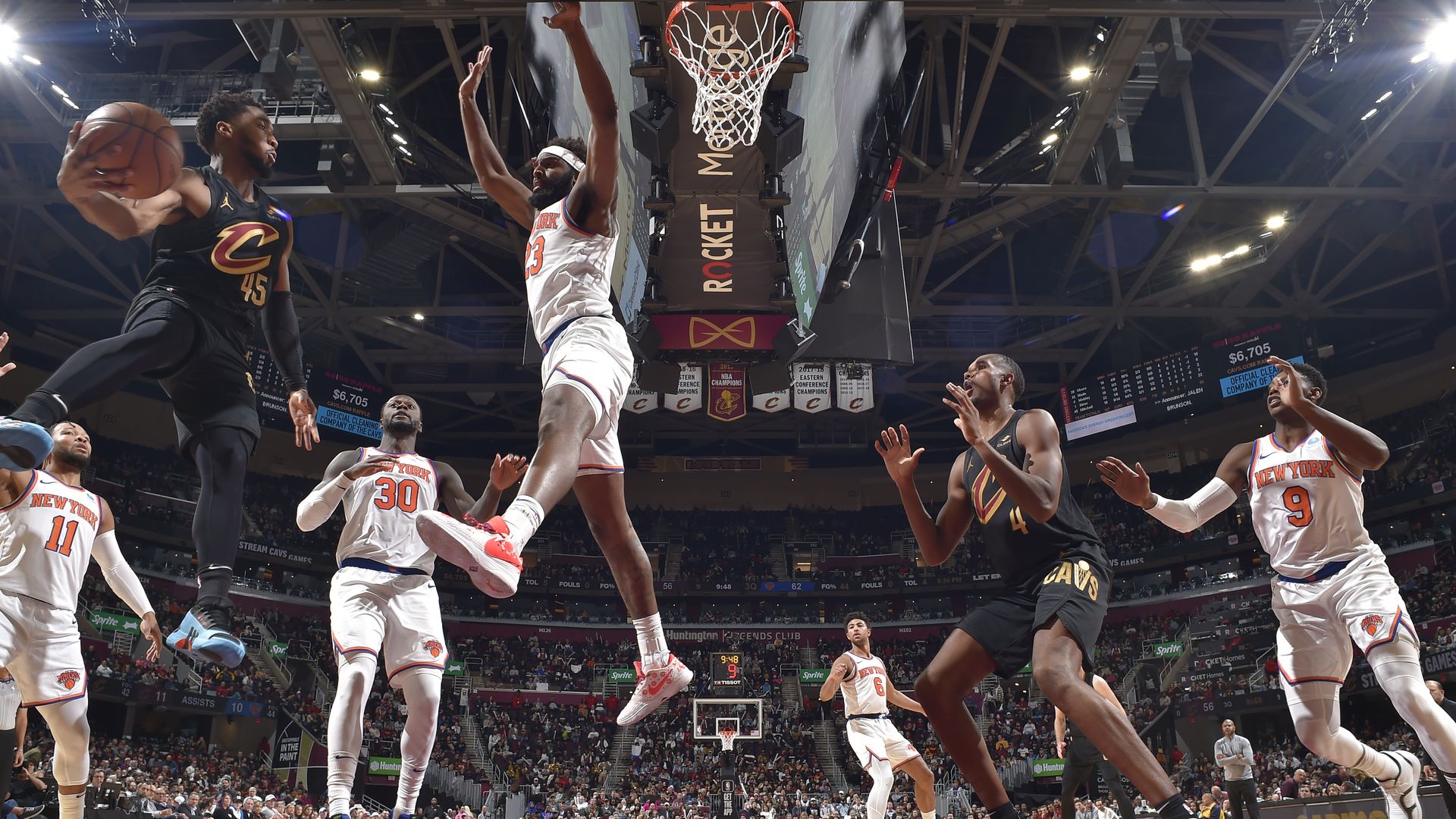Donovan Mitchell attempts to pass to Evan Mobley under the basket, while the Knicks in white uniforms play defense.