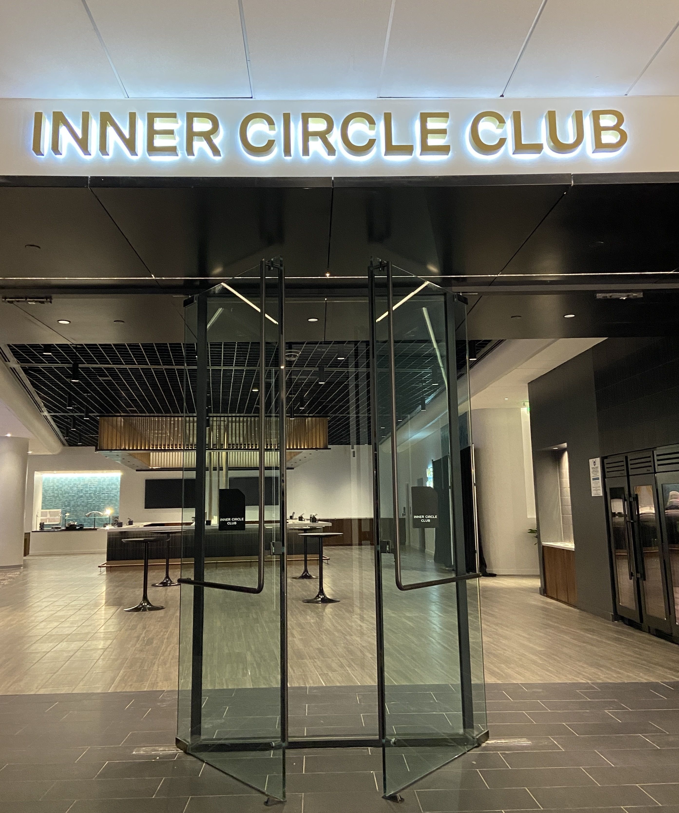 Glass entrance doors to the INNER CIRCLE CLUB, illuminated sign above, showing an interior with wood flooring, tables, and modern lighting.