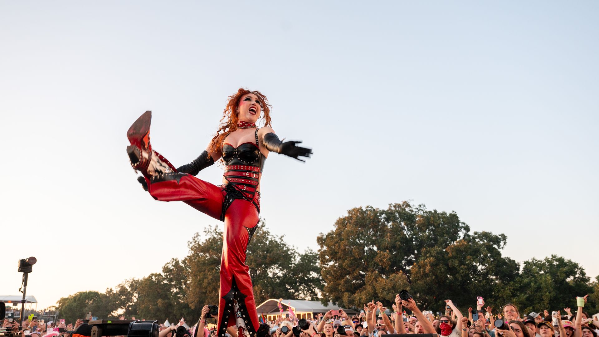 Chappell Roan kicks on stage in a red outfit with the crowd dancin gin the background.
