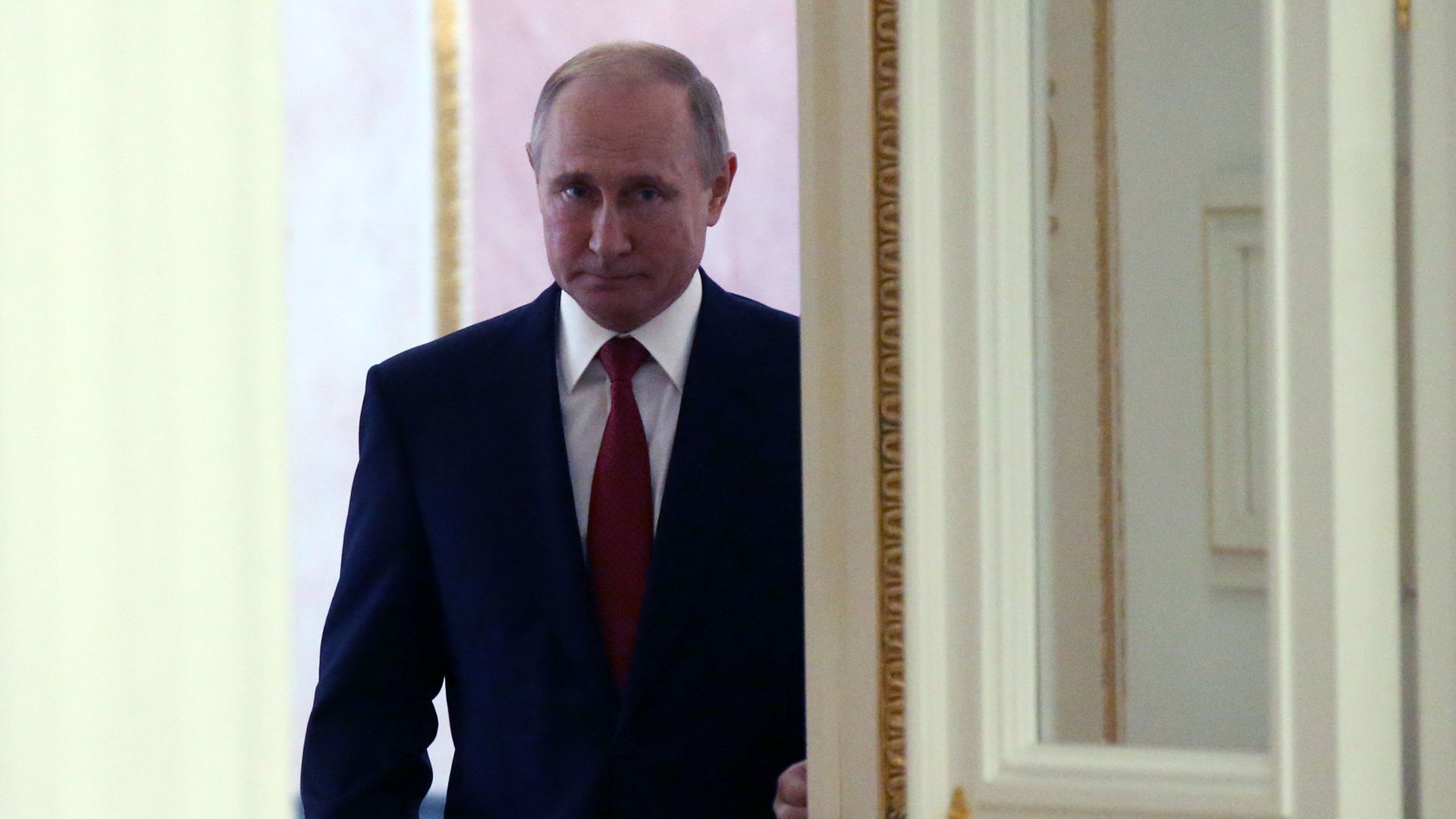 Vladimir Putin stands near a door and looks meek.