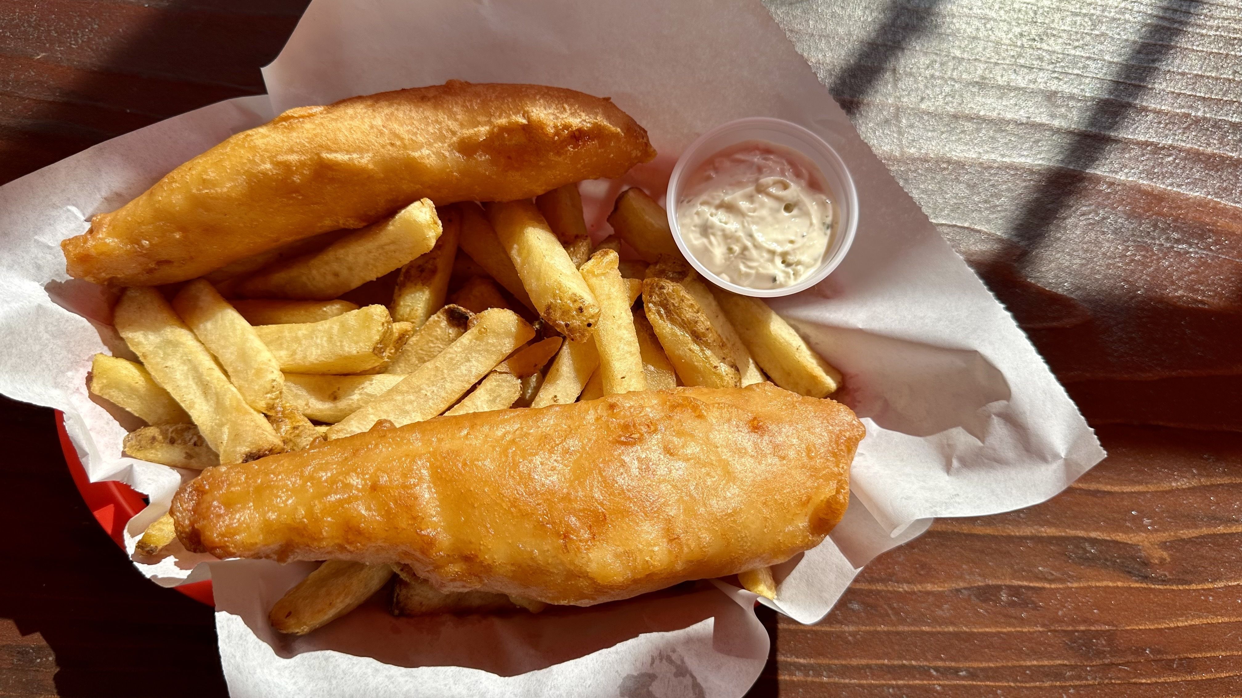 A photo of two golden fish pieces on a bed of fries in a paper-filled basket.