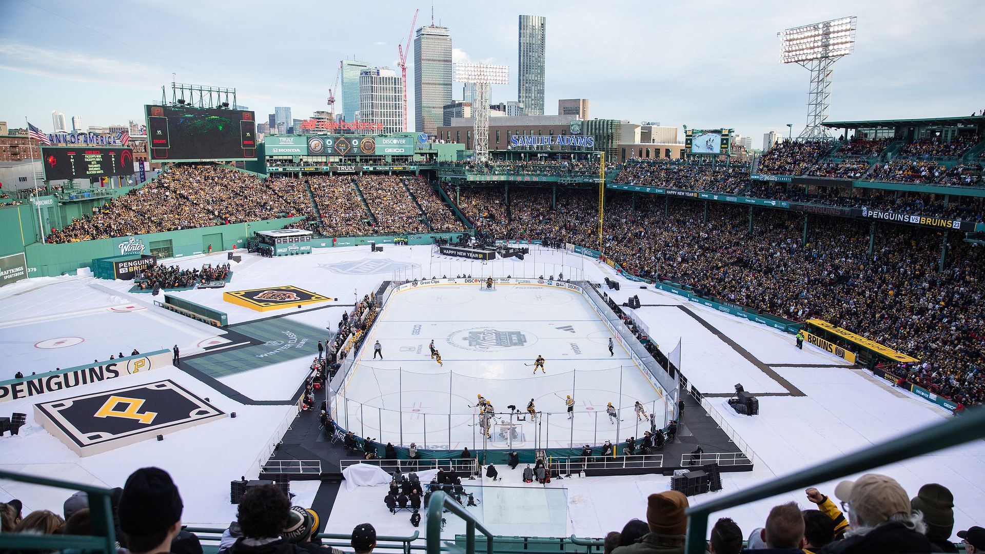 An ice rink sites upon Fenway Park's field during the Winter Classic. This is the view from the stands with the Prudential Center and other skyscrapers in the background.