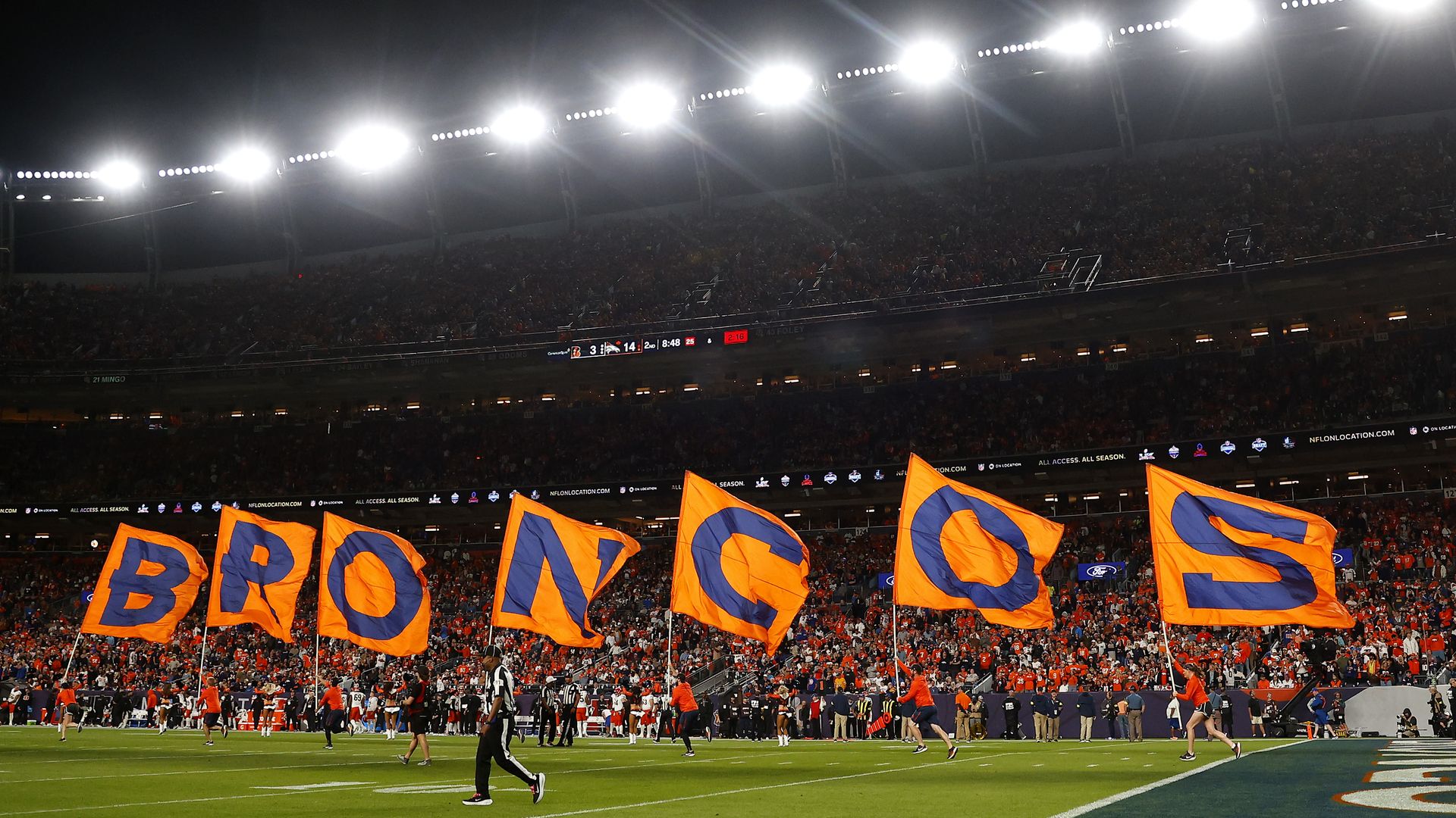 People holding flags that spell out BRONCOS while being lit by stadium lights. 