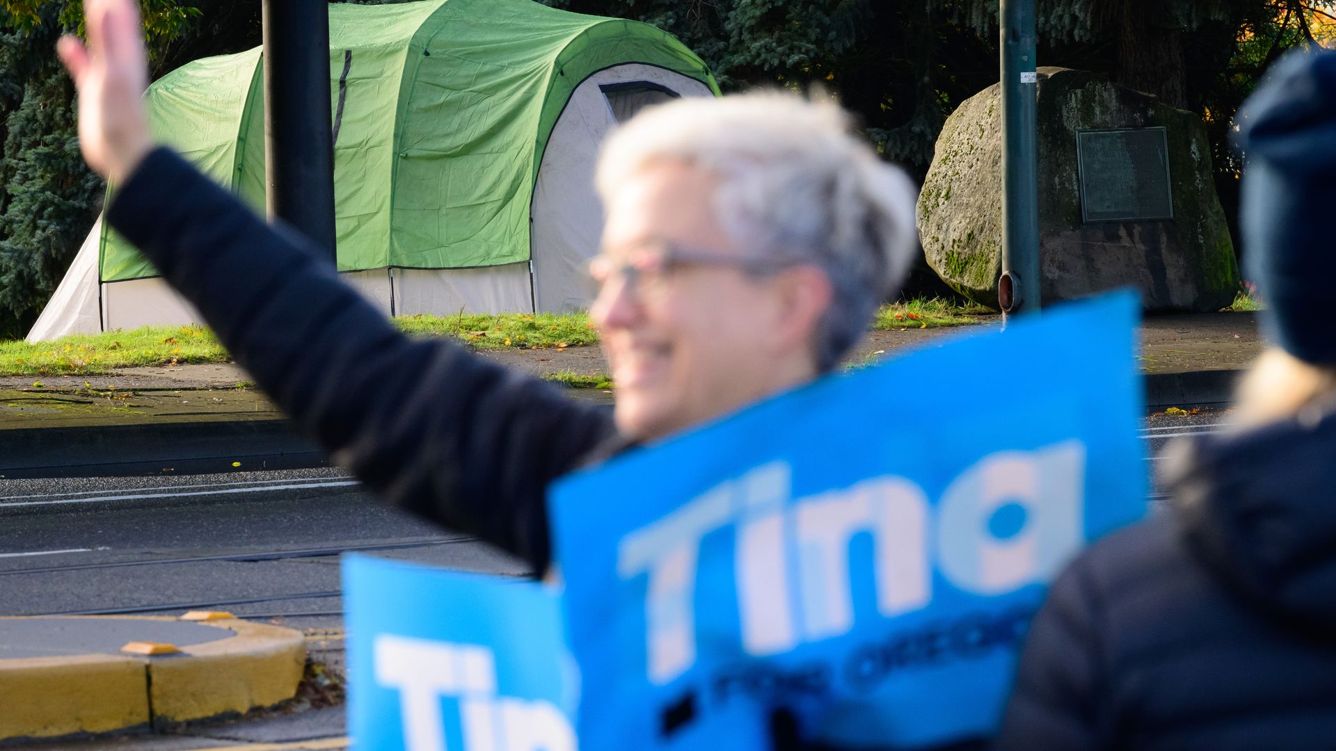 Gov. tina Kotek stands outside campaigning and holding a sign.