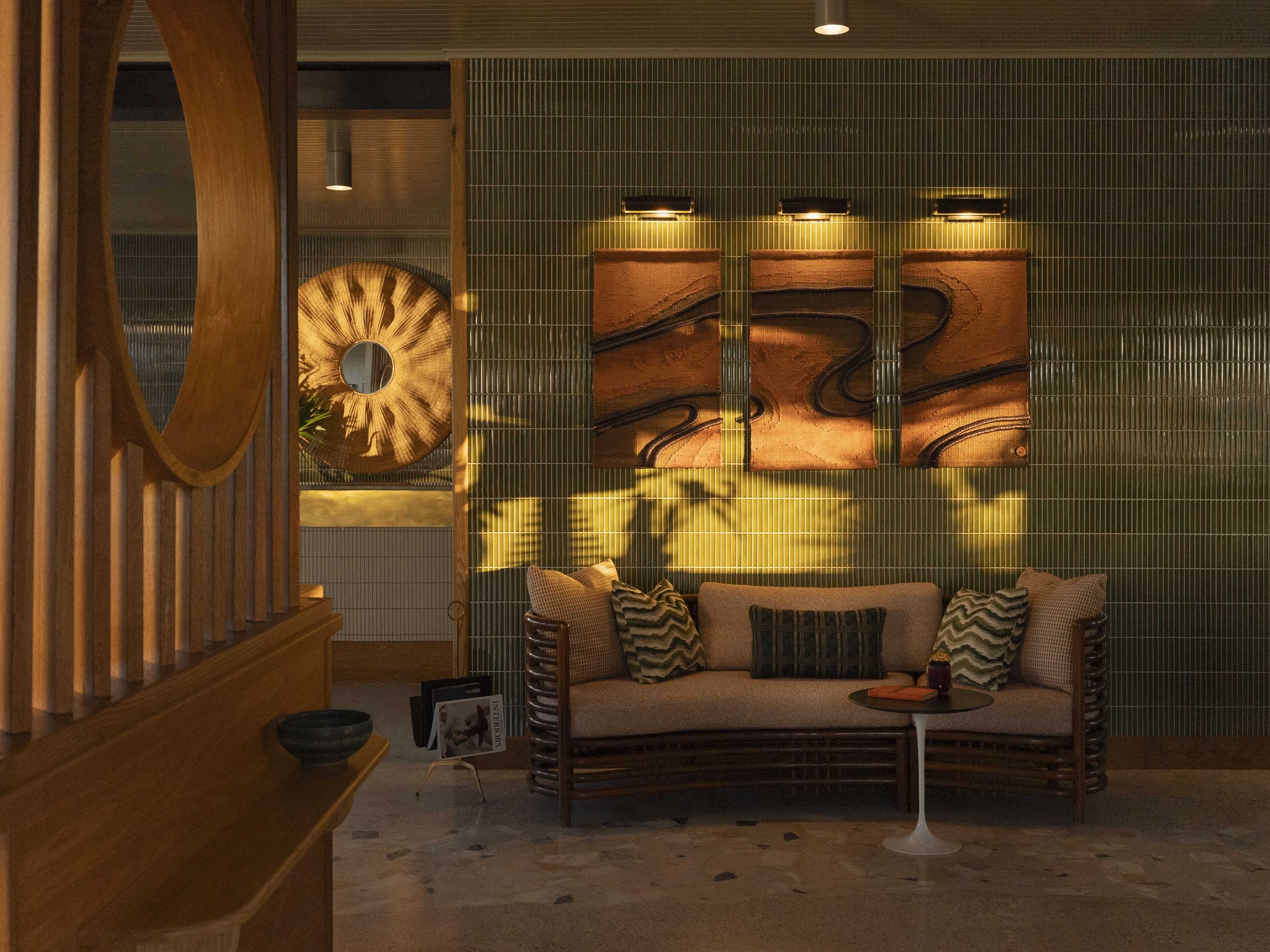 A green tiled wall has wooden art work on it. A lounging couch sits underneath.