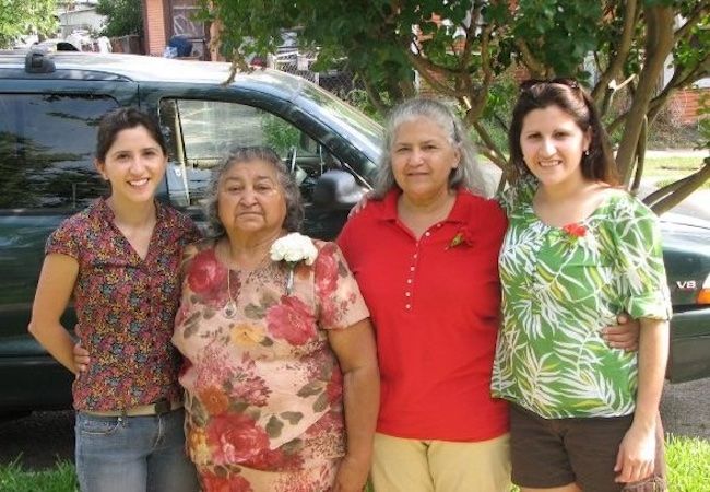 Four women from the same family stand side by side in front of a dark green SUV. 