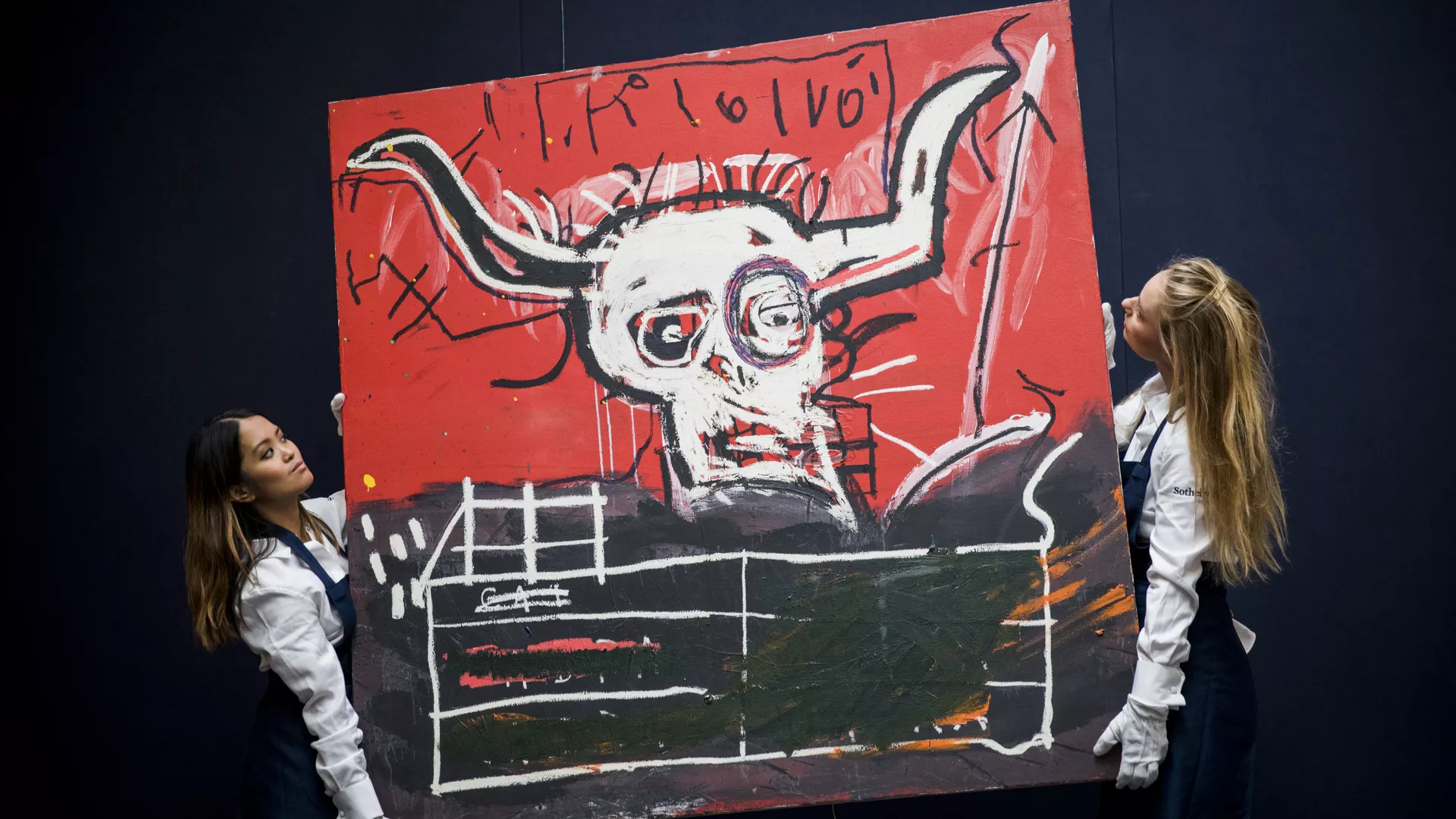Two women hold up a large painting of a creature with horns