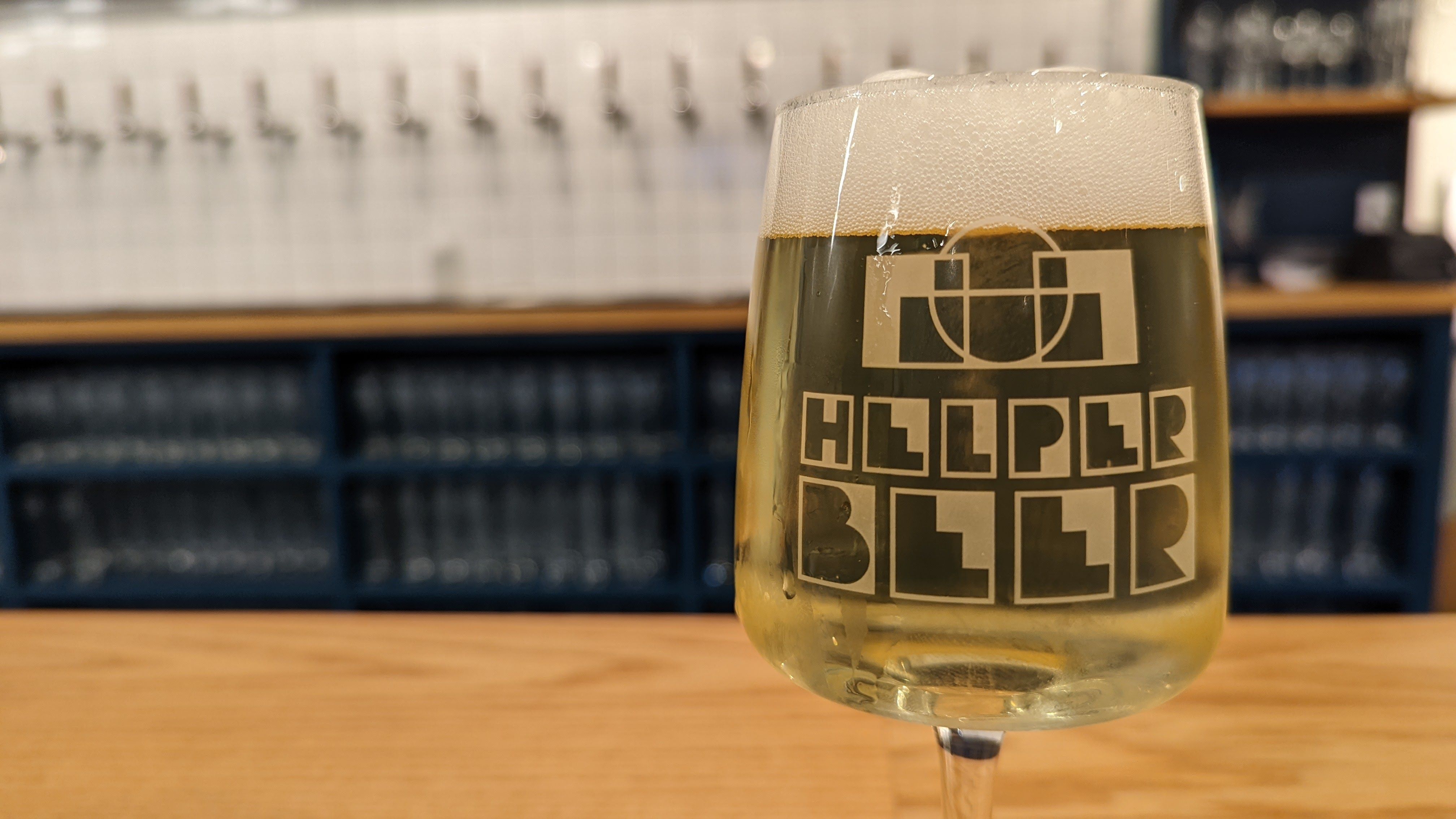 A glass of beer, etched with a logo that reads "Helper Beer"