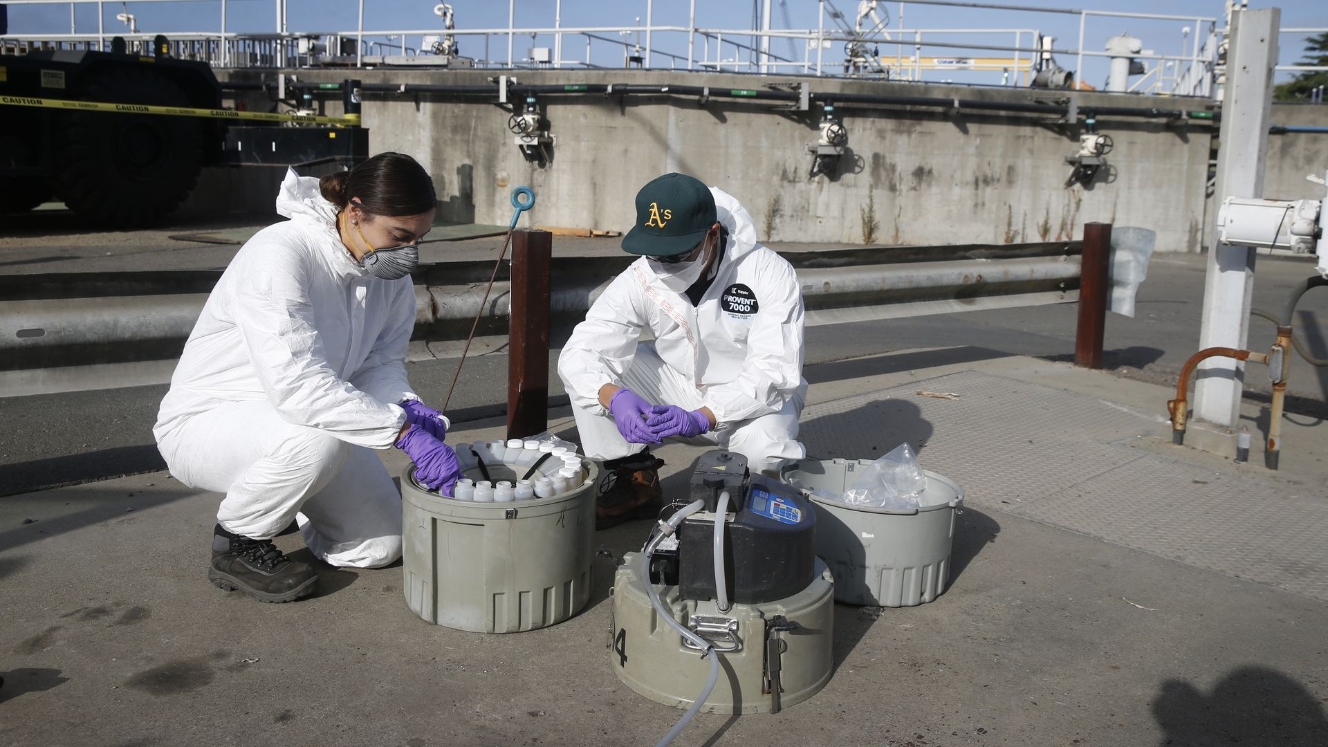 Photo of two people in PPE squatting over two containers of sample bottles at a wastewater plant