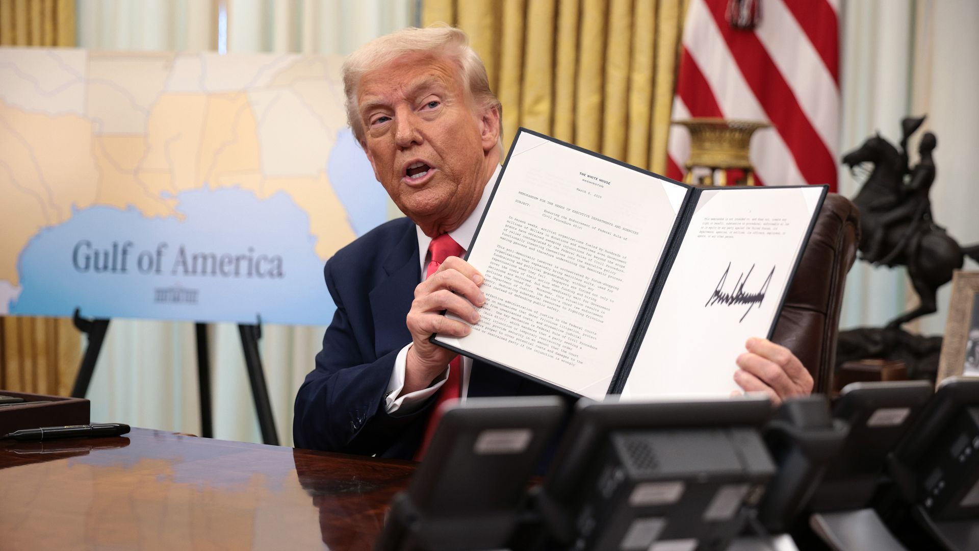 Trump holds up a signed executive order. A map reading "Gulf of America" is visible behind him.