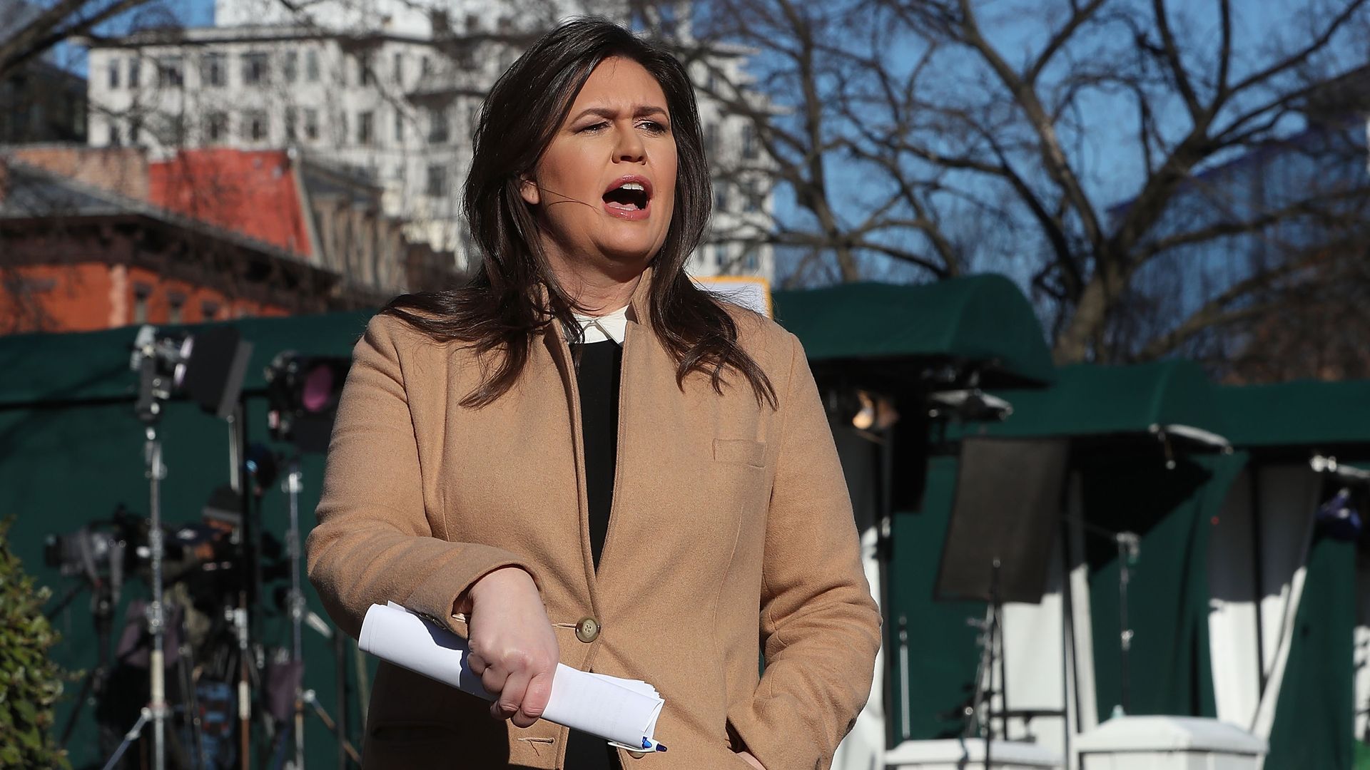 Sarah Sanders talking to reporters with a beige coat on. 