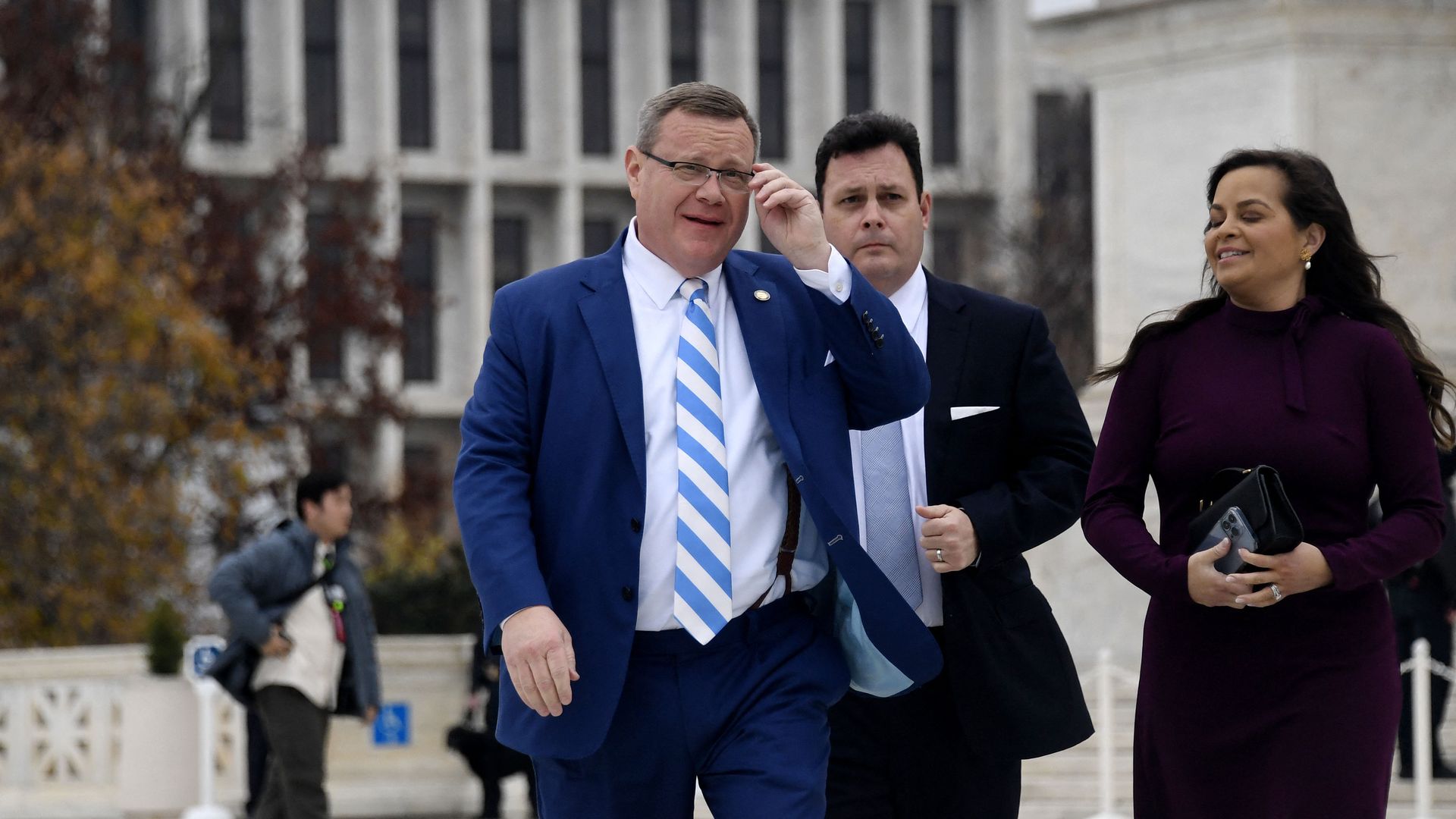 North Carolina House Speaker Tim Moore in a blue suit with a blue and white tie, walking with two people.