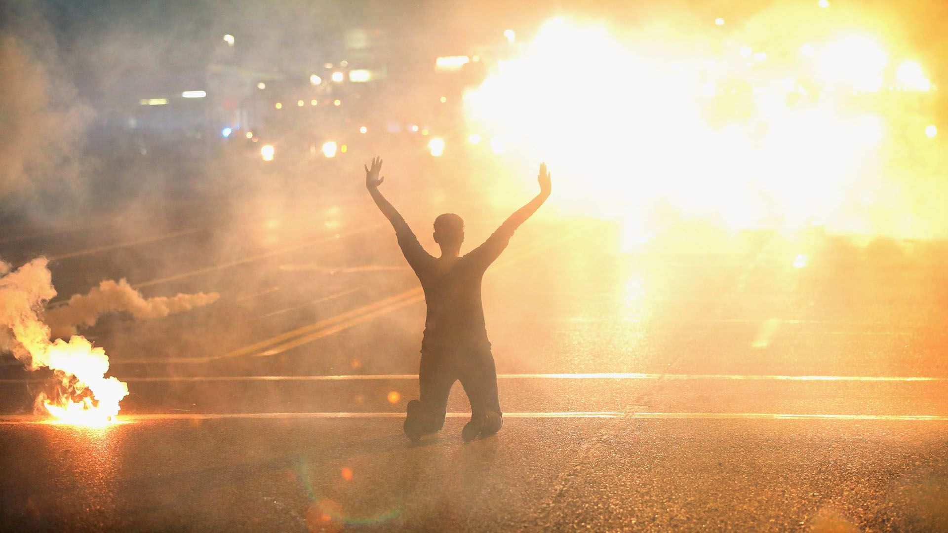 A woman kneels on the streets as police spray tear gas on her