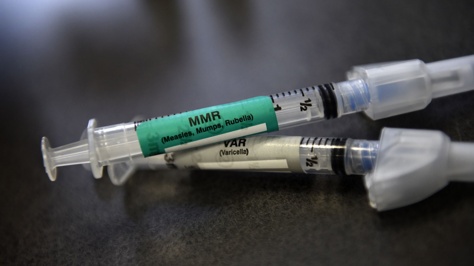 In this image, two syringes for the MMR vaccine are laying on top of each other on a table.