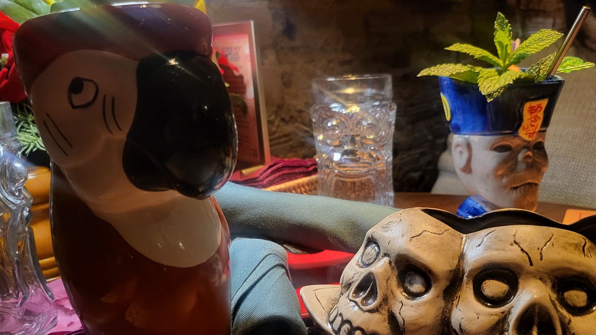 A parrot mug next to two fake skulls in a tiki bar.