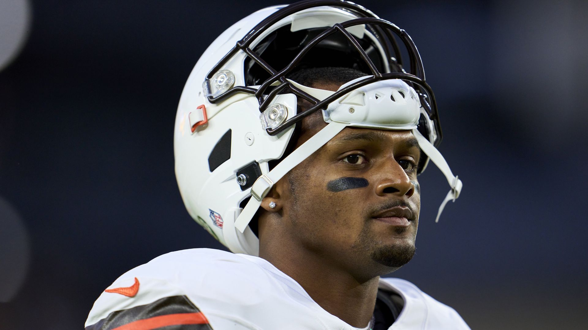Browns quarterback Deshaun Watson stands on the field with his helmet resting on the top of his head.