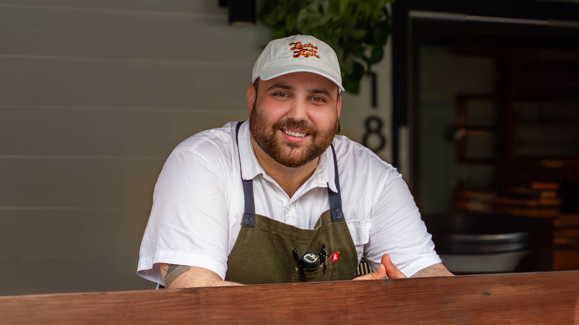 Emil Oliva stands in front of his restaurant wearing an apron and baseball cap. 