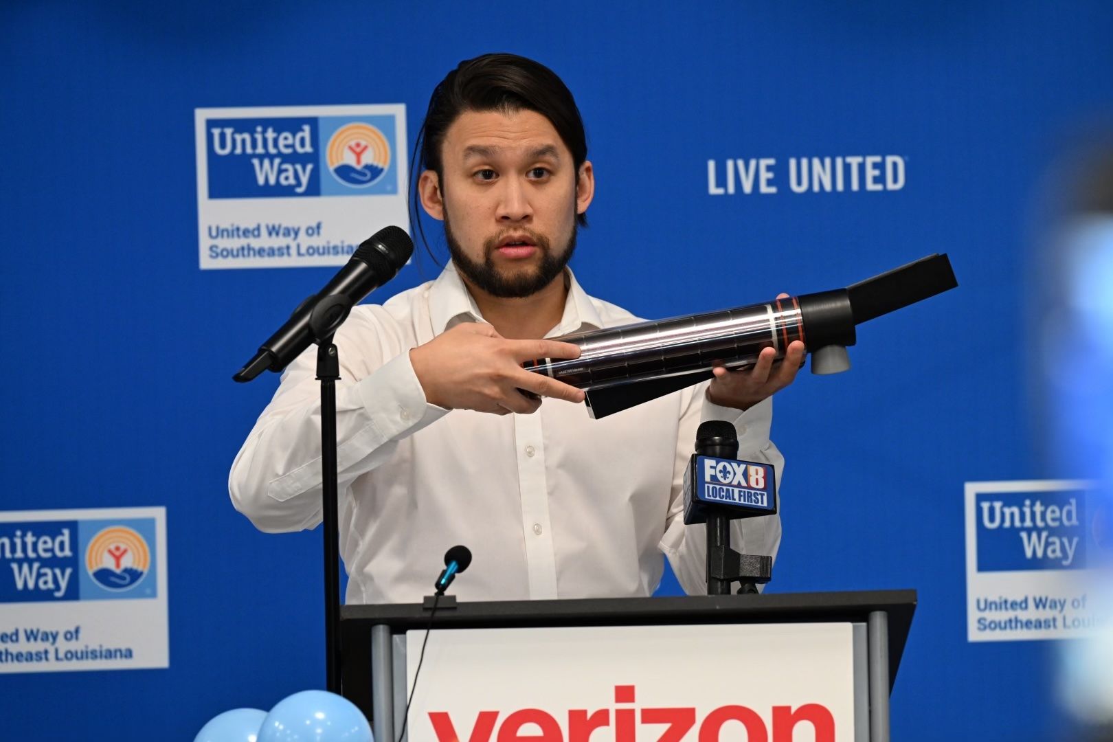 Brandon Wong stands at a podium as he holds up a black, tube-like sensor.