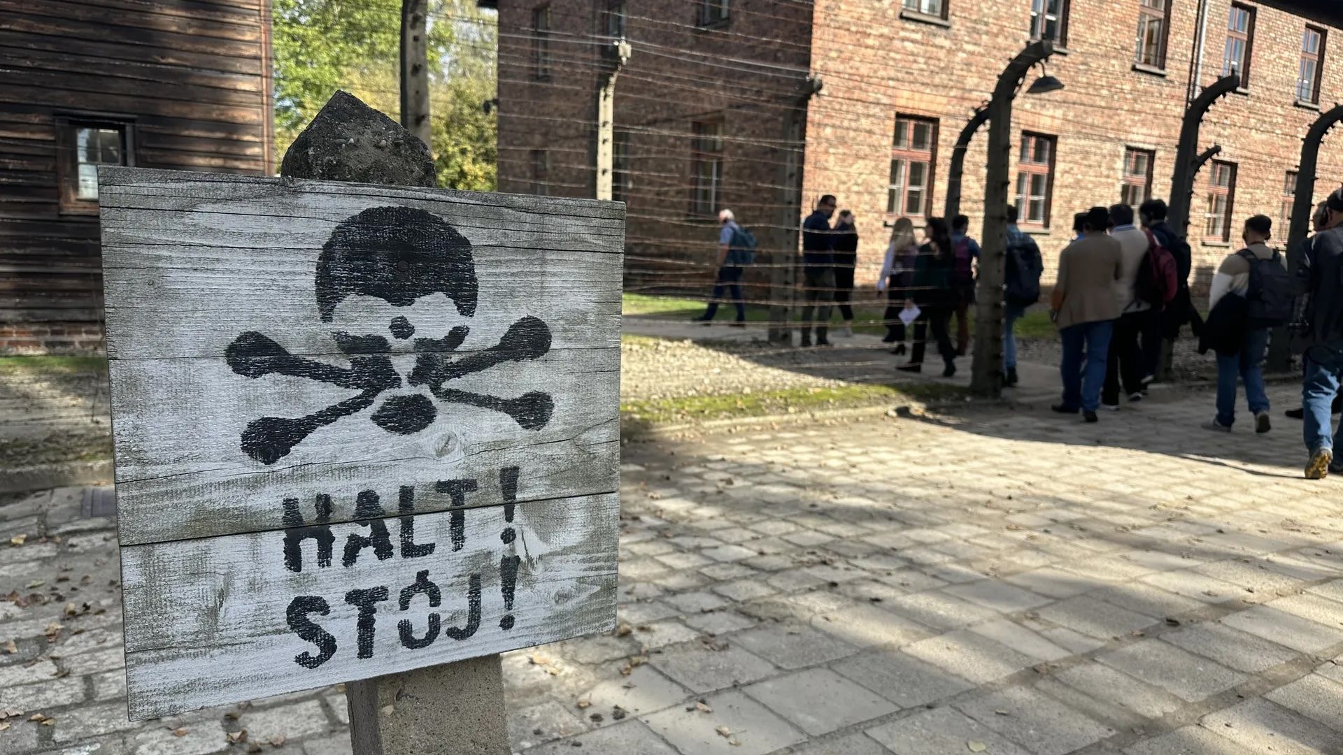 Visitors to Auschwitz-Birkenau Memorial & Museum on Oct. 8, 2024 tour barracks around a stop sign that used to warn prisoners to stay away from an electric fence. Photo: Russell Contreras/Axios