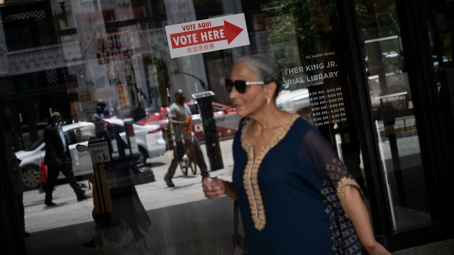 A person walks past the MLK Memorial Library entrance, where a poster that says "VOTE HERE" points visitors toward a polling center