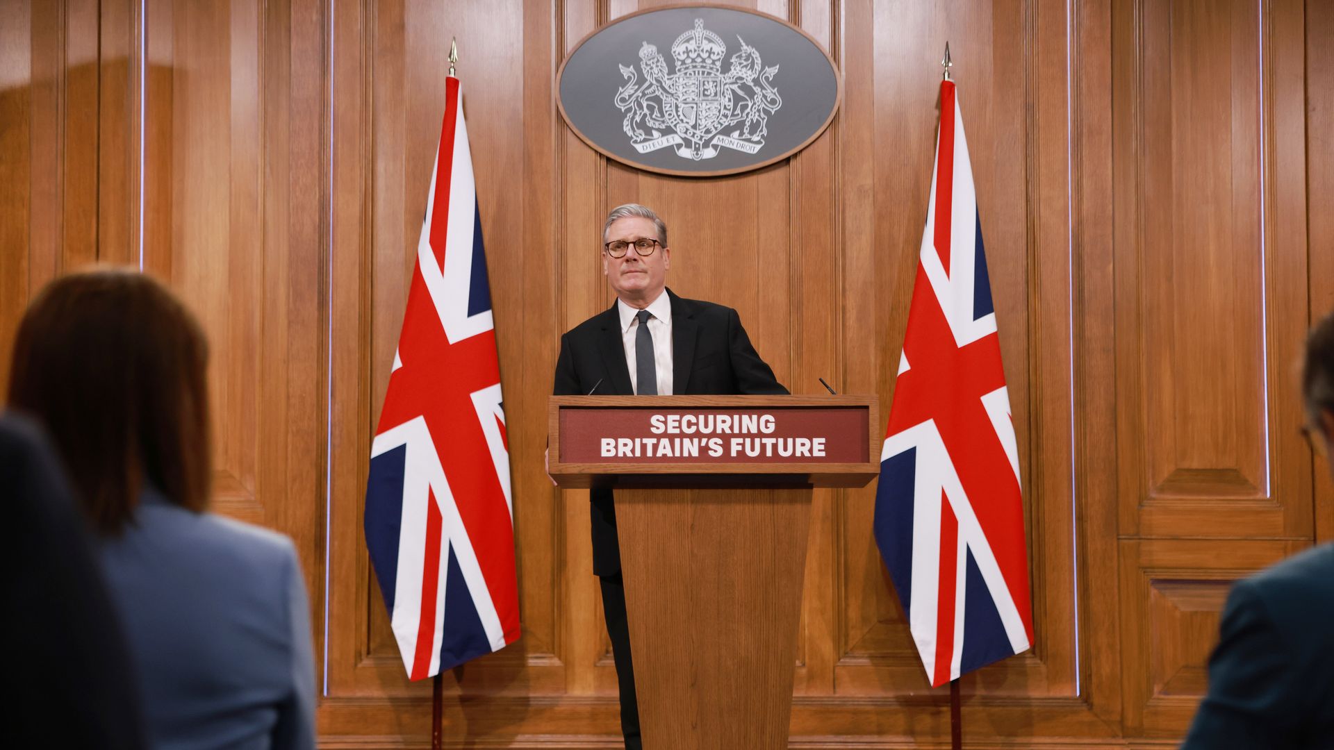 Keir Starmer stands at a lectern flanked by two union jacks. In front of him, a sign reads "securing Britain's future." 