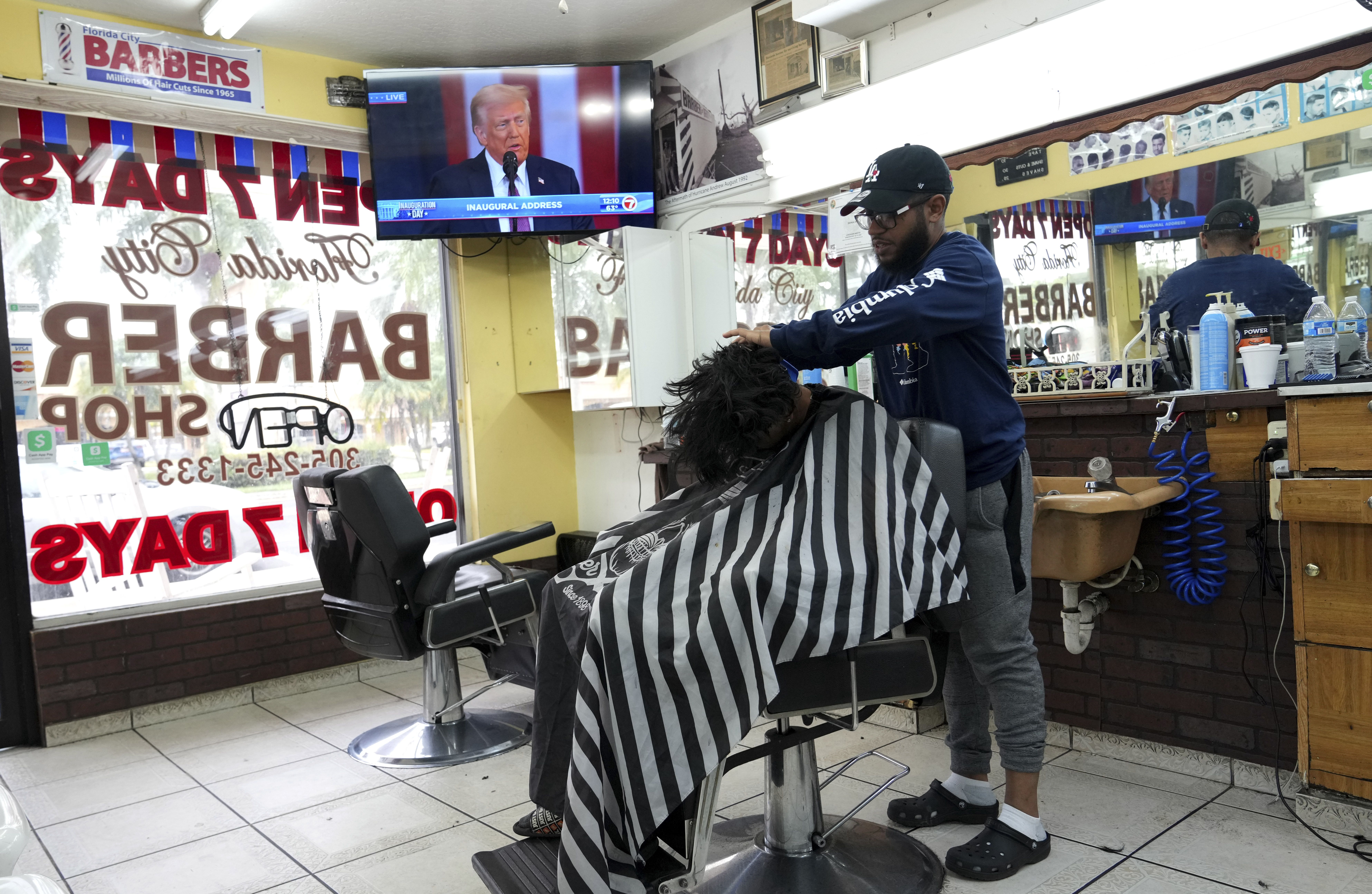 Jose Silvestre, right, styles a customer's hair at Florida City Barbers in Florida City, Fla. as Donald Trump gives his inaugural address after being sworn in as the 47th president of the United States Monday, Jan. 20, 2025. (AP Photo/Lynne Sladky)