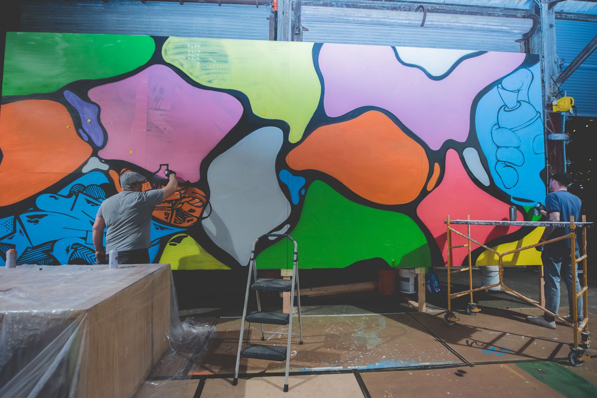 Artists paint a colorful mural on plywood.