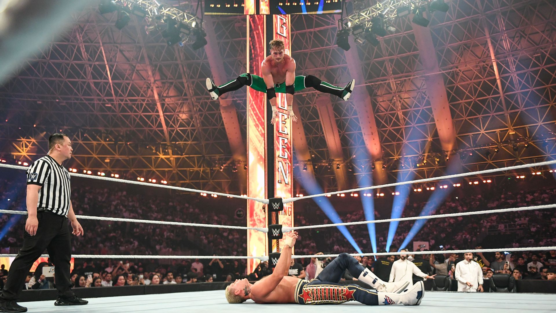 WWE's Logan Paul jumps from the top rope towards Cody Rhodes on the mat. 