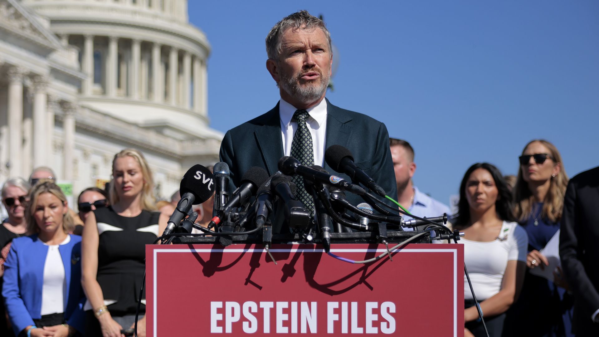 Rep. Thomas Massie speaks at a podium outside the U.S. Capitol with alleged Epstein victims standing behind him.