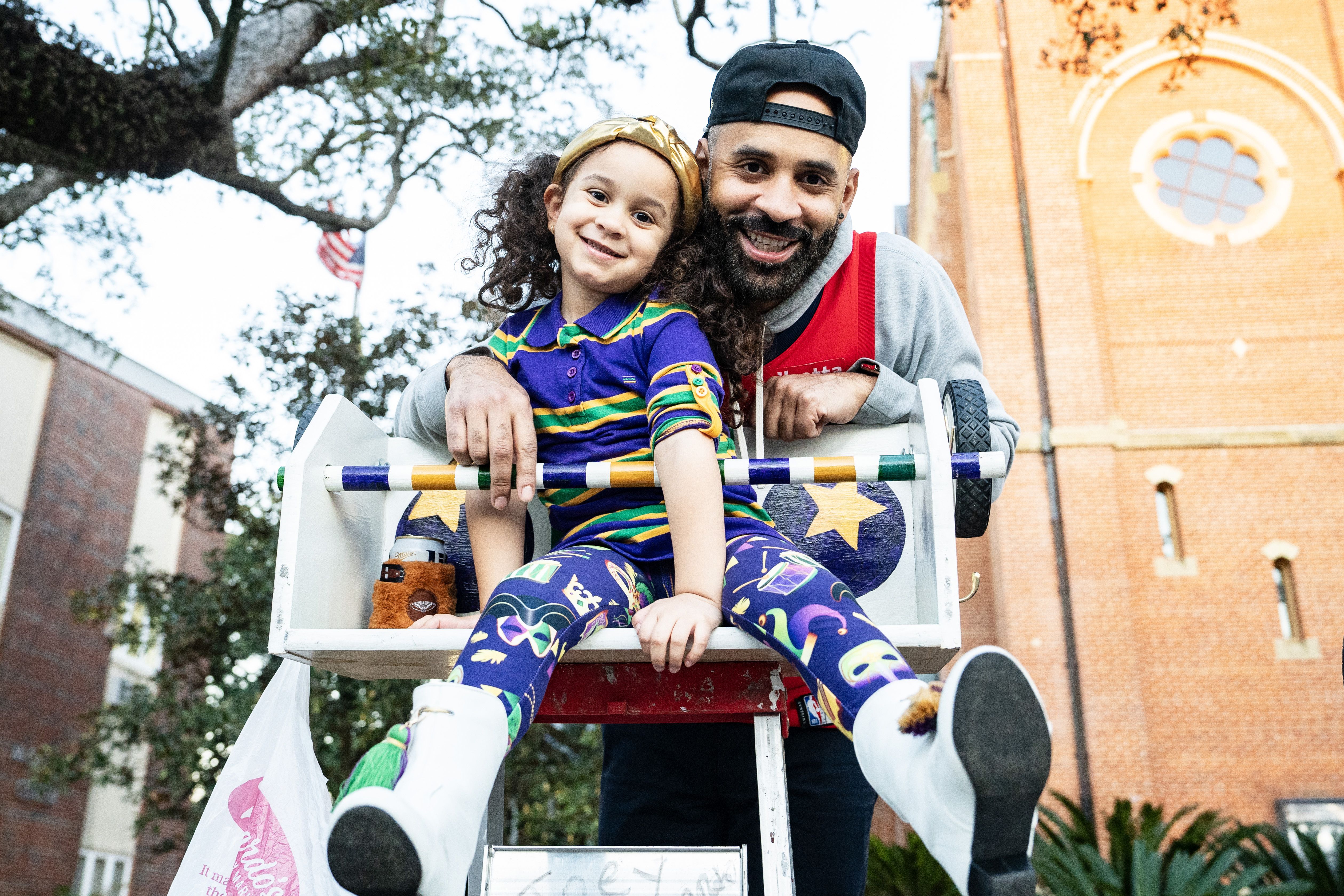 A man smiles over his child's shoulder atop a parade ladder.